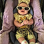Nylah is registered to the contest to win money with this photo: baby, sunglasses, headband, car_seat, plush, toy, purple, yellow, clothing, infant, smile, hands, socks, cute, comfort, seat_cover, animal_toy, patterned_pants, indoor, relaxed