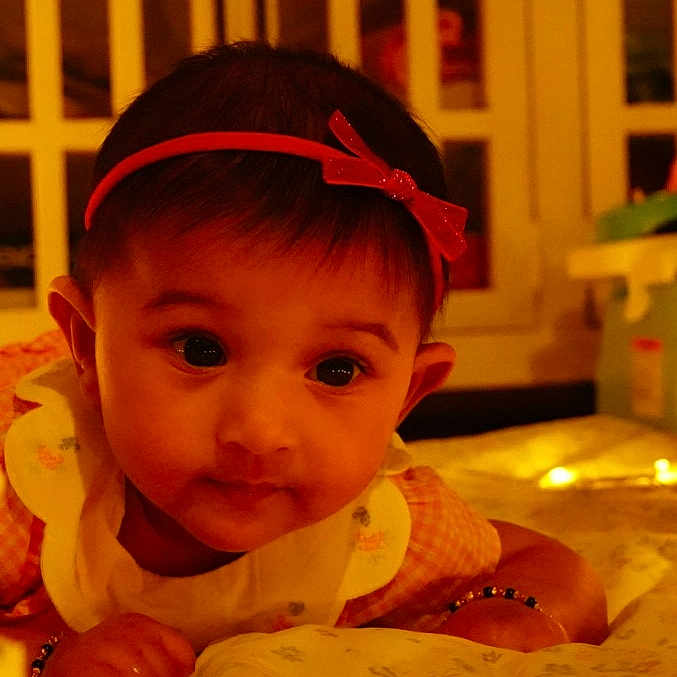 Trishika joined the competition — help win amazing prizes! baby, bed, blanket, bracelet, child, closeup, curious, cute, face, headband, indoors, infant, portrait, red_bow, resting, sleepwear, soft_light, tummy, warm_lighting, young_child