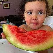Eleanor is registered to the contest to win money with this photo: child, toddler, watermelon, food, fruit, messy_face, high_chair, indoor, curly_hair, big_eyes, snack_time, summer_food, healthy_eating, close_up, person, cute, eating, table, home, background