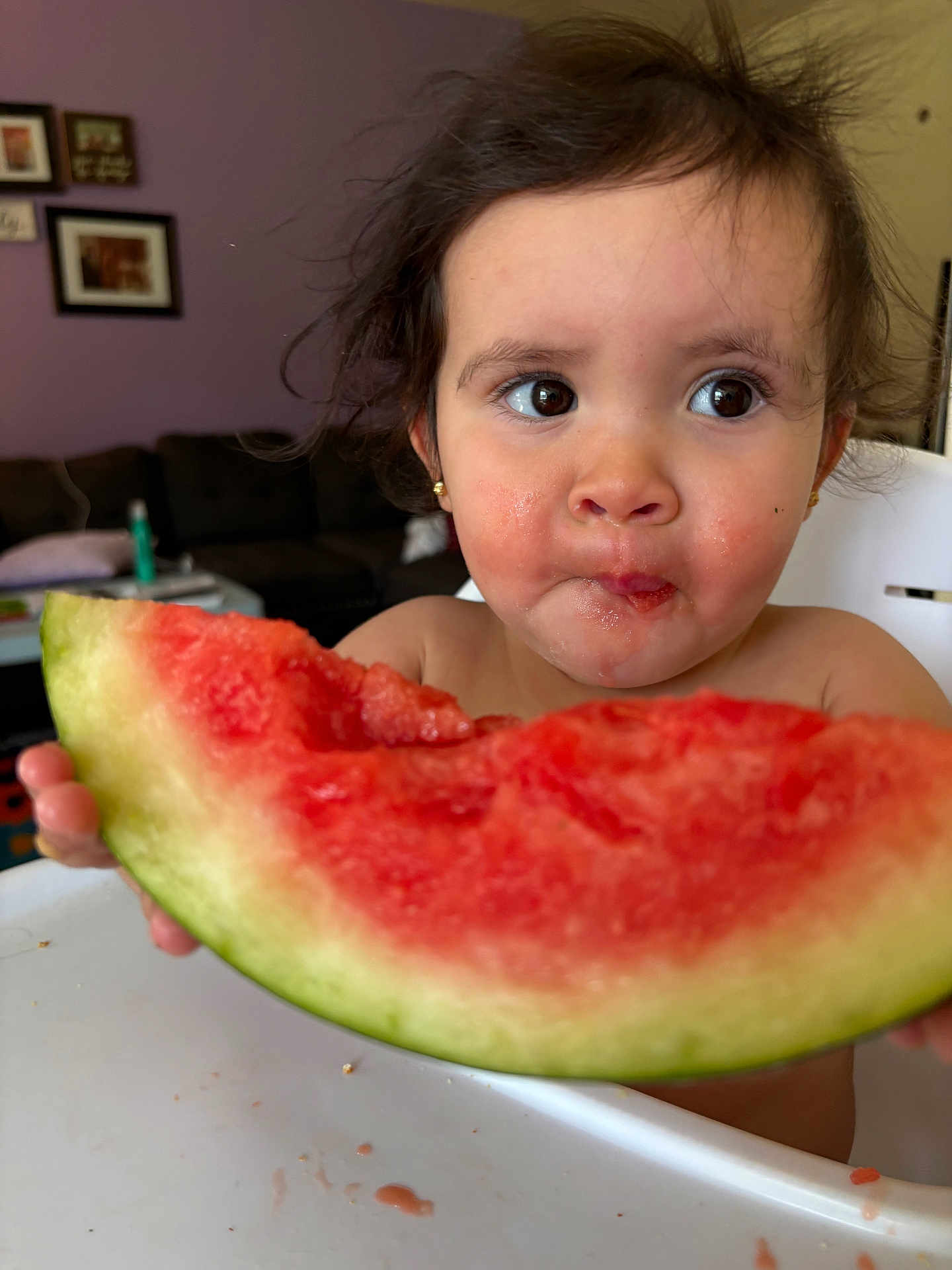 Eleanor is registered to the contest to win money with this photo: child, toddler, watermelon, food, fruit, messy_face, high_chair, indoor, curly_hair, big_eyes, snack_time, summer_food, healthy_eating, close_up, person, cute, eating, table, home, background
