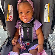 Naylani is registered to the contest to win money with this photo: baby, child, car_seat, headband, bow, purple_outfit, pacifier, blanket, pink, smiling, tongue_out, straps, cute, infant, sitting, indoors, playful, happy, person, young