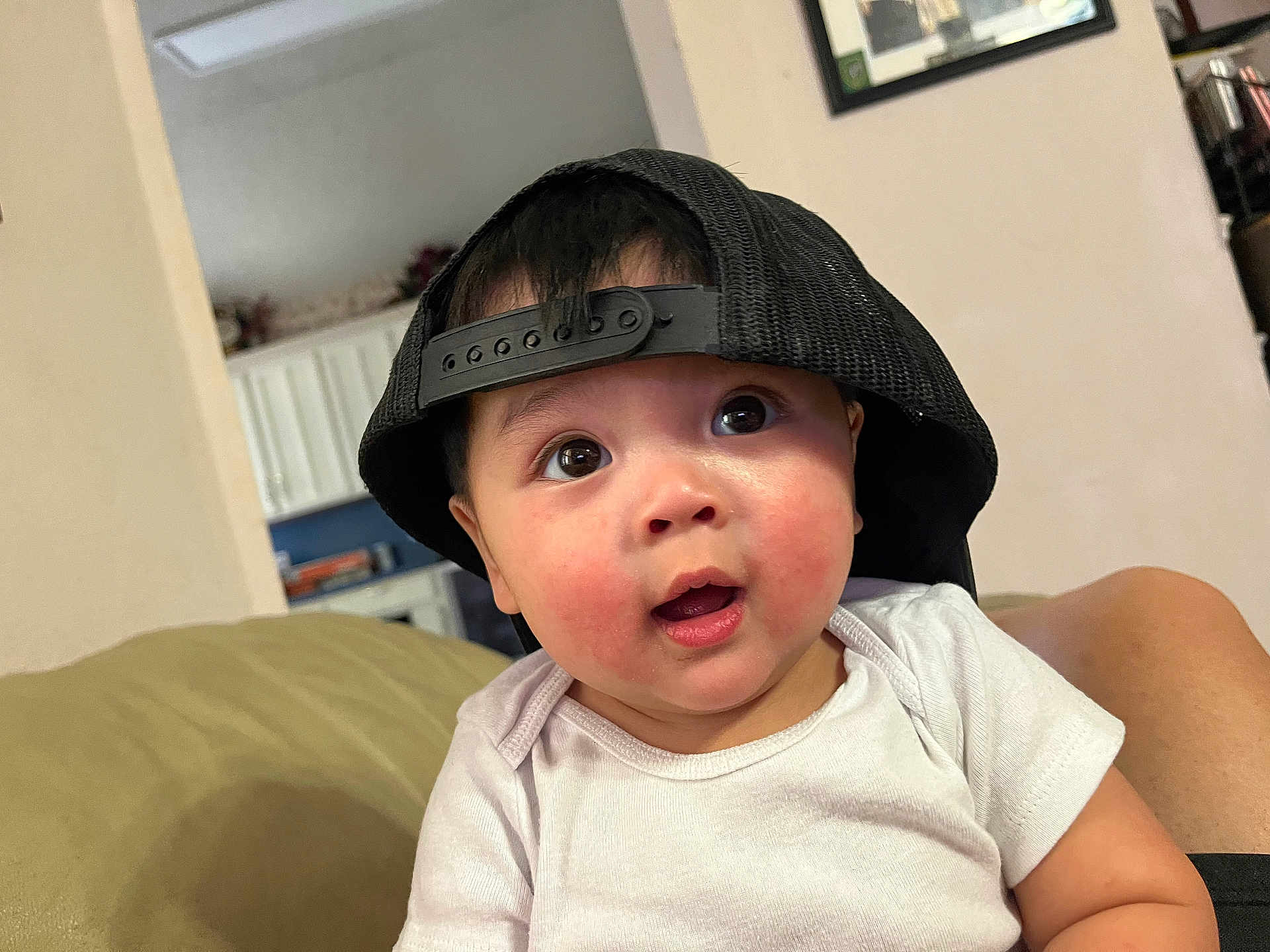 Lincoln joined the competition — help win amazing prizes! baby, child, cap, hat, indoor, couch, white_shirt, curious, wide_eyes, face, person, infant, skin, cheeks, short_sleeve, furniture, living_room, casual, portrait, cute