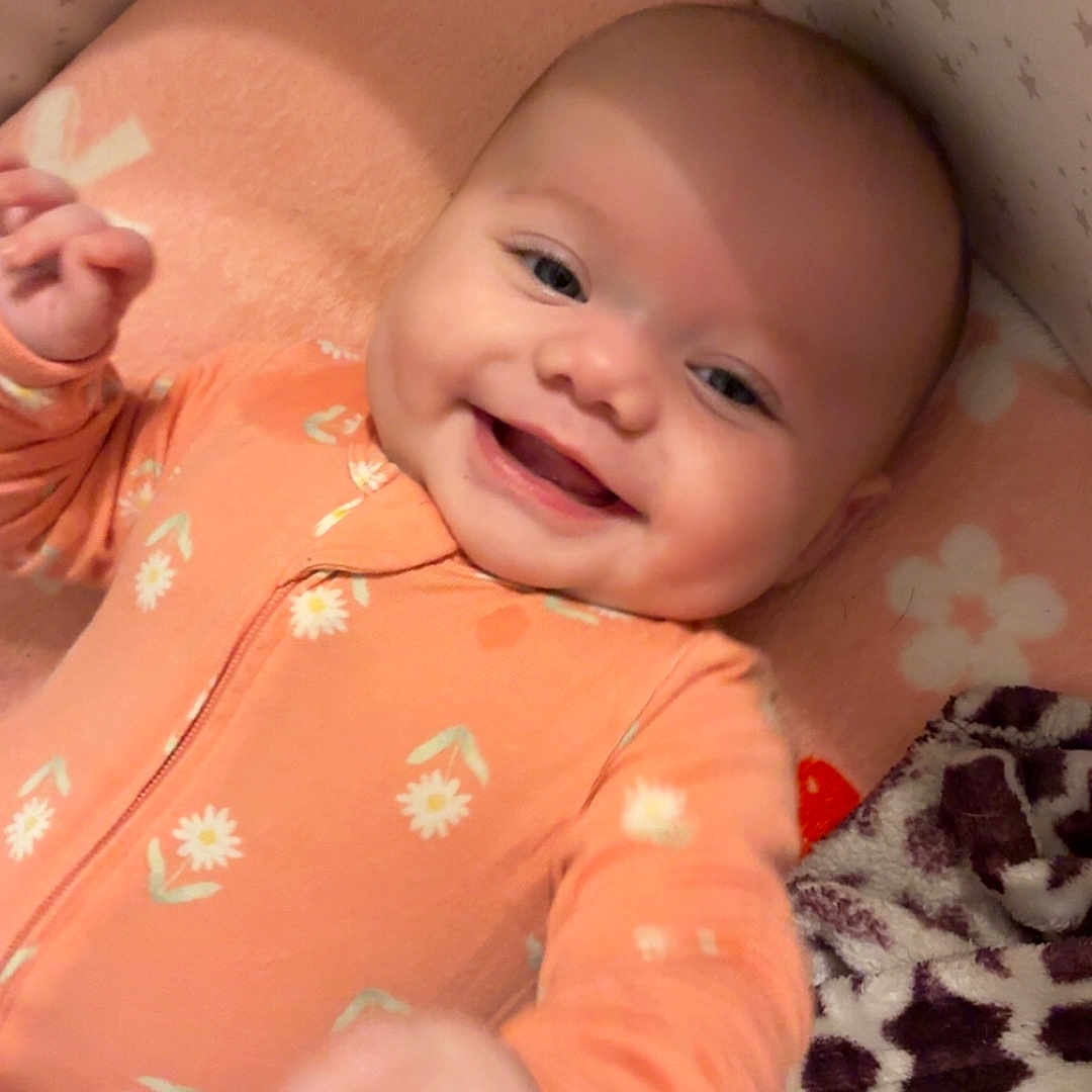 Lakelee is registered to the contest to win money with this photo: baby, blanket, child, comfort, cozy, cute, face, flower_pattern, hand, happy, indoors, infant, lying_down, nursery, orange_onesie, pacifier, smiling, soft_toys, star_wallpaper, strawberry_pattern