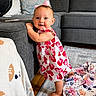 baby, child, girl, standing, smiling, pink_bow, strawberry_dress, couch, living_room, blanket, cushion, floor, carpet, wooden_floor, happy, indoor, portrait, furniture, home, cute