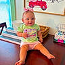 baby, child, pink_bow, green_shirt, new_balance, pink_shorts, table, wooden_table, basket, wall_art, red_truck, blessed_text, indoors, smiling, cute, sitting, person, face, happy, decor
