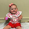 baby, child, smile, pink_bow, red_shorts, cherry_pattern, toy, purple_egg, sitting, blanket, happy, indoor, cute, portrait, infant, clothing, person, face, hands, feet