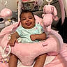 baby, infant, child, plush_toy, pink, soft_toy, baby_seat, cushion, smiling, tongue_out, indoor, laundry_basket, clothing, green_shirt, person, cute, playful, legs, feet, furniture