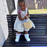 Milani joined the competition — help win amazing prizes! child, girl, standing, bench, white_dress, braided_hair, beads, handbag, sneakers, socks, outdoor, fence, window, wall, grass, sunlight, smile, portrait, accessories, fashion