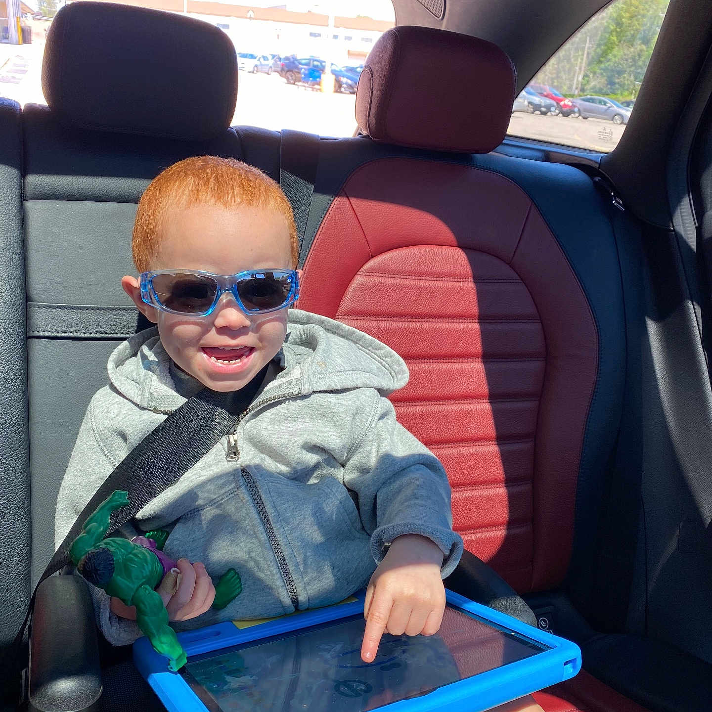 Grayson joined the competition — help win amazing prizes! action_figure, car_interior, car_seat, casual_clothing, child, daylight, happy, hoodie, playing, red_hair, seat, seatbelt, smiling, sunglasses, sunlight, tablet, technology, toy, window, young_child