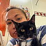 Gojo is registered to the contest to win money with this photo: person, cat, black_cat, tuxedo_cat, indoor, bathroom, selfie, pet, collar, bell, whiskers, face, hair, shelf, toiletries, tile_wall, curious, closeup, casual, striped_clothing