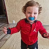 black_pants, carpet, child, curly_hair, cute, doorway, floor, happy, home, indoor, pacifier, person, playful, red_jacket, smiling, sporty, standing, toddler, wall, young_child
