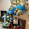 Ibrahim participe au concours pour gagner de l'argent avec cette photo : balloons, banner, birthday, blue_balloons, celebration, child, clothing, curly_hair, door, floor_rug, gift_wrap, gold_balloons, indoor, party_decorations, presents, red_car, television, toddler, toy_car, white_balloons