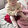 toddler, child, bed, blanket, clothing, curly_hair, sock, pink, red, white, knitwear, indoor, soft_light, pacifier, furniture, curtain, radiator, floor, person, playing