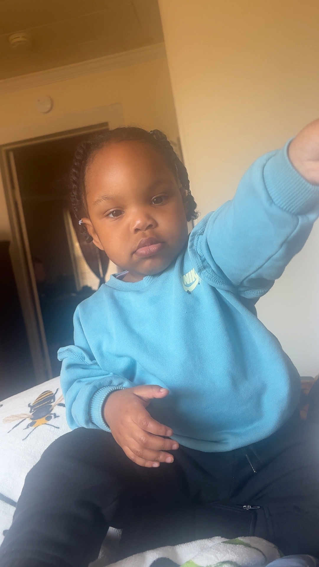 Raya joined the competition — help win amazing prizes! toddler, child, blue_sweatshirt, braided_hair, indoor, bed, blanket, bee_pattern, hand, face, person, curious, casual_clothing, young_child, portrait, sitting, room, door, furniture, calm_expression