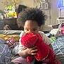 child, plush_toy, elmo, bed, blanket, indoor, hair, clothing, person, toy, furniture, room, sitting, hand, face, footwear, decor, television, door, cushion