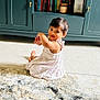 toddler, child, white_dress, carpet, rug, indoor, cabinet, books, furniture, curly_hair, person, carpet_pattern, floor, sitting, looking_back, home, cozy, cute, young_child, living_room