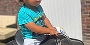 Louka a rejoint le concours — aidez-le/la à gagner de superbes lots ! child, toddler, curly_hair, blue_shirt, panda_pants, saddle, outdoor, sunlight, brick_wall, white_door, bench, footwear, focused, cute, young_child, playful, casual_clothing, daylight, person, portrait