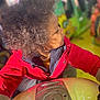 child, curly_hair, red_jacket, ride, amusement_park, colorful, indoor, play, portrait, side_profile, young, fun, vibrant, clothing, person, activity, focus, light, blurred_background, casual