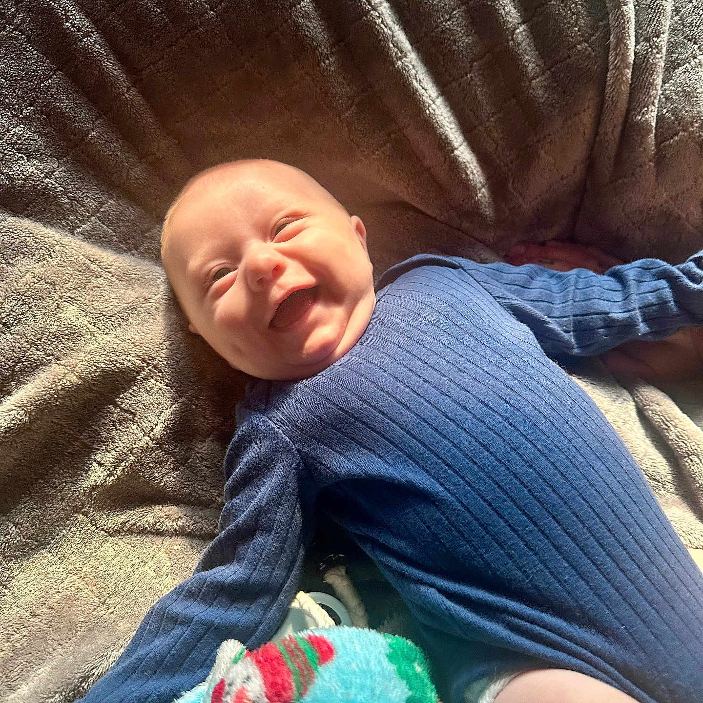 Grayson joined the competition — help win amazing prizes! baby, smiling, blue_outfit, blanket, cozy, texture, soft, sunlight, happy, infant, lying_down, cute, child, indoors, warm_light, blanket_pattern, comfort, portrait, playful, relaxed