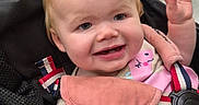 Luna is registered to the contest to win money with this photo: baby, child, infant, smiling, happy, stroller, seated, waving, hands, face, portrait, indoor, clothing, pink, harness, safety_belt, blonde_hair, blue_eyes, baby_carrier, family_outing