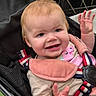 baby, child, infant, smiling, happy, stroller, seated, waving, hands, face, portrait, indoor, clothing, pink, harness, safety_belt, blonde_hair, blue_eyes, baby_carrier, family_outing