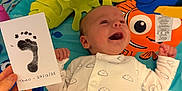 Theo joined the competition — help win amazing prizes! baby, infant, onesie, footprint, hand, play_mat, toy, smile, happy, child, indoor, colorful, cute, person, young, face, clothing, pattern, lying_down, celebration