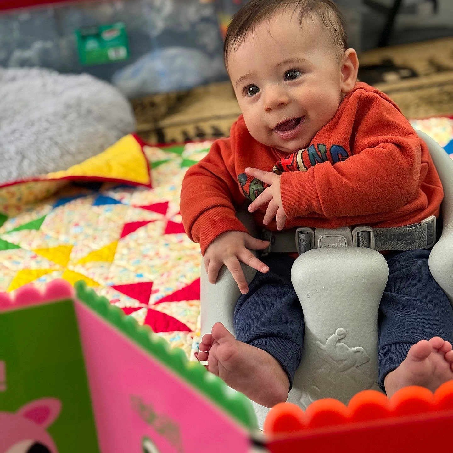 Leland is registered to the contest to win money with this photo: baby, bodypart, clothing, couch, cushion, face, finger, furniture, hand, happy, head, homedecor, indoors, pants, person, photography, portrait, quilt, sitting, smile