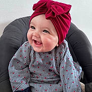Esméralda participe au concours pour gagner de l'argent avec cette photo : baby, child, smiling, red_headwrap, bow, patterned_clothing, seated, cushion, indoor, happy, cute, portrait, infant, chubby_cheeks, long_sleeves, buttoned_shirt, bright, warm, closeup, face