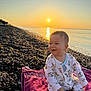 Mattias is registered to the contest to win money with this photo: baby, child, sunset, beach, pebbles, towel, smiling, onesie, sea, water, sun, outdoor, nature, happy, infant, sky, sand, sunlight, relaxation, portrait