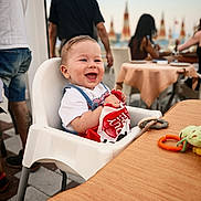 Mattias joined the competition — help win amazing prizes! baby, high_chair, smiling, child, outdoor, dining, table, toy, person, happy, plastic_bag, short_sleeve_shirt, people, restaurant, summer, daylight, casual, food, seat, background