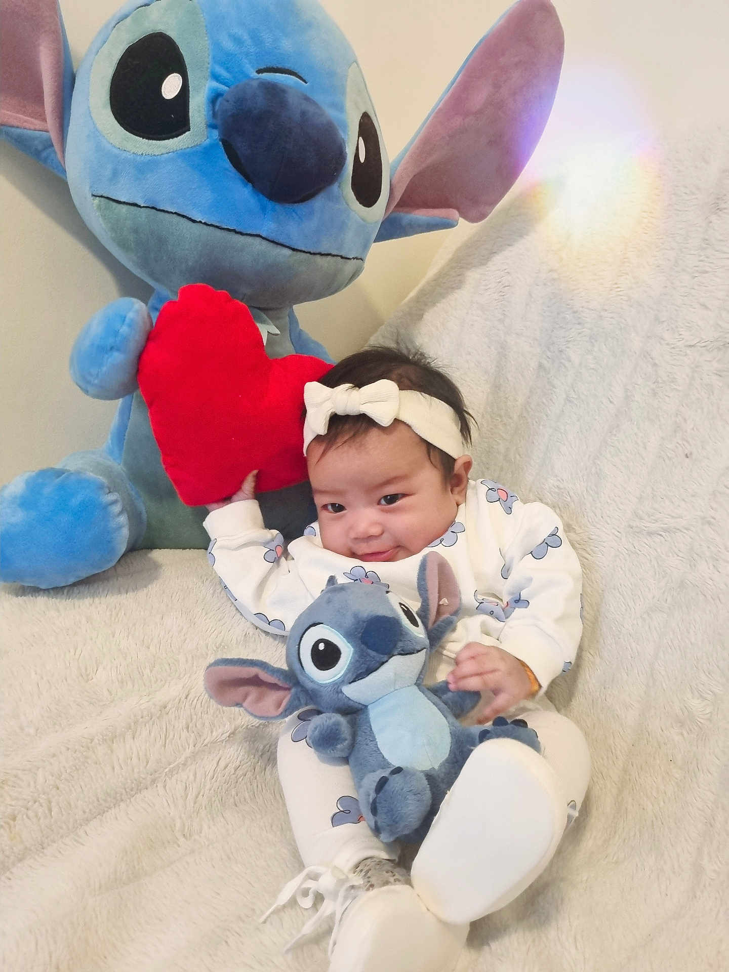 Olivia participe au concours pour gagner de l'argent avec cette photo : baby, blanket, child, couch, cozy, cute, flower_pattern, headband, heart, indoor, infant, plush_toy, red_heart, seated, smile, soft_texture, stitch, stuffed_animal, toy, white_outfit