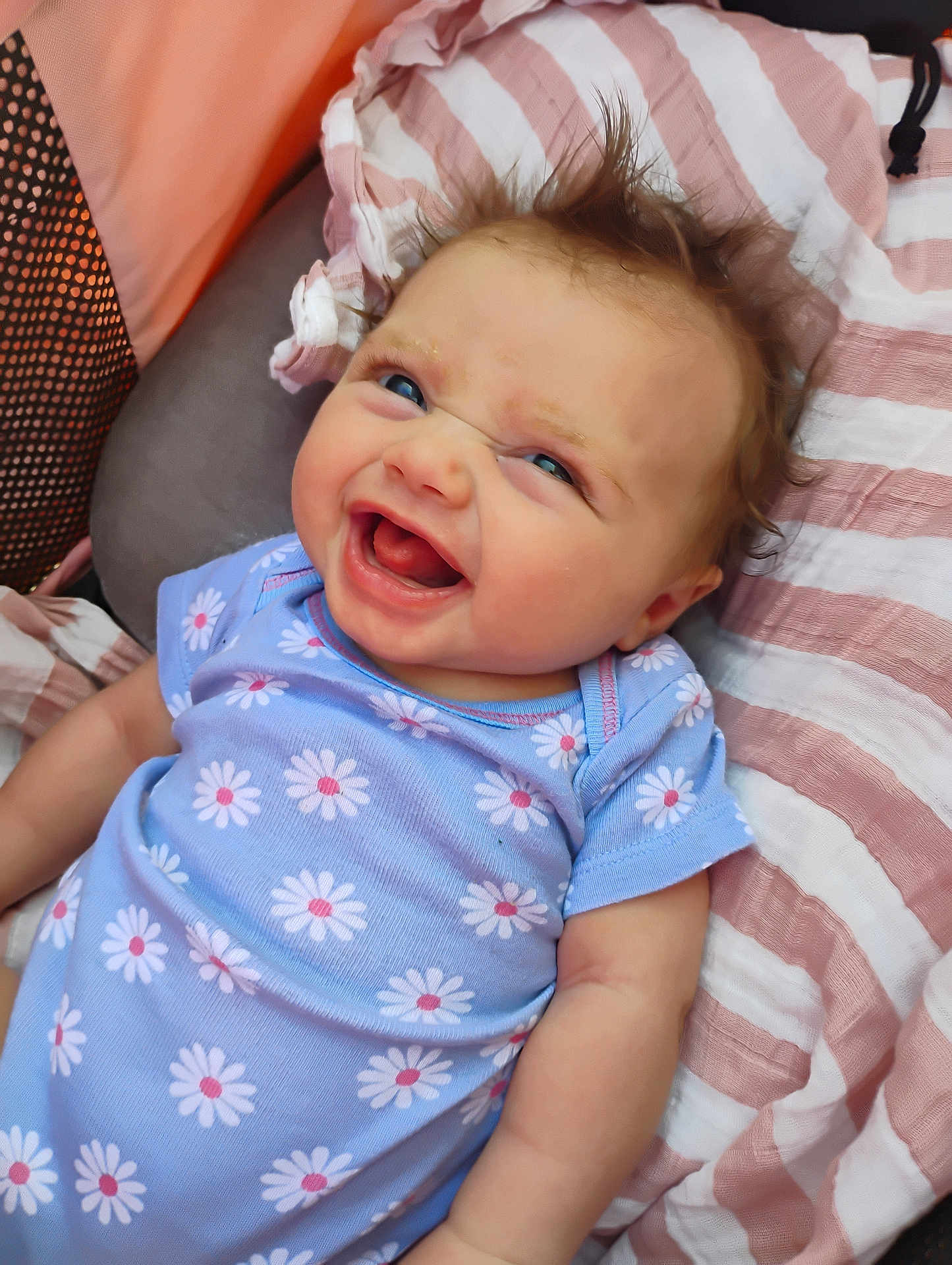 Harper is registered to the contest to win money with this photo: baby, child, smiling, laughing, blue_onesie, daisies, hair, blanket, striped, pink, white, face, happy, infant, cute, lying_down, skin, person, closeup, portrait