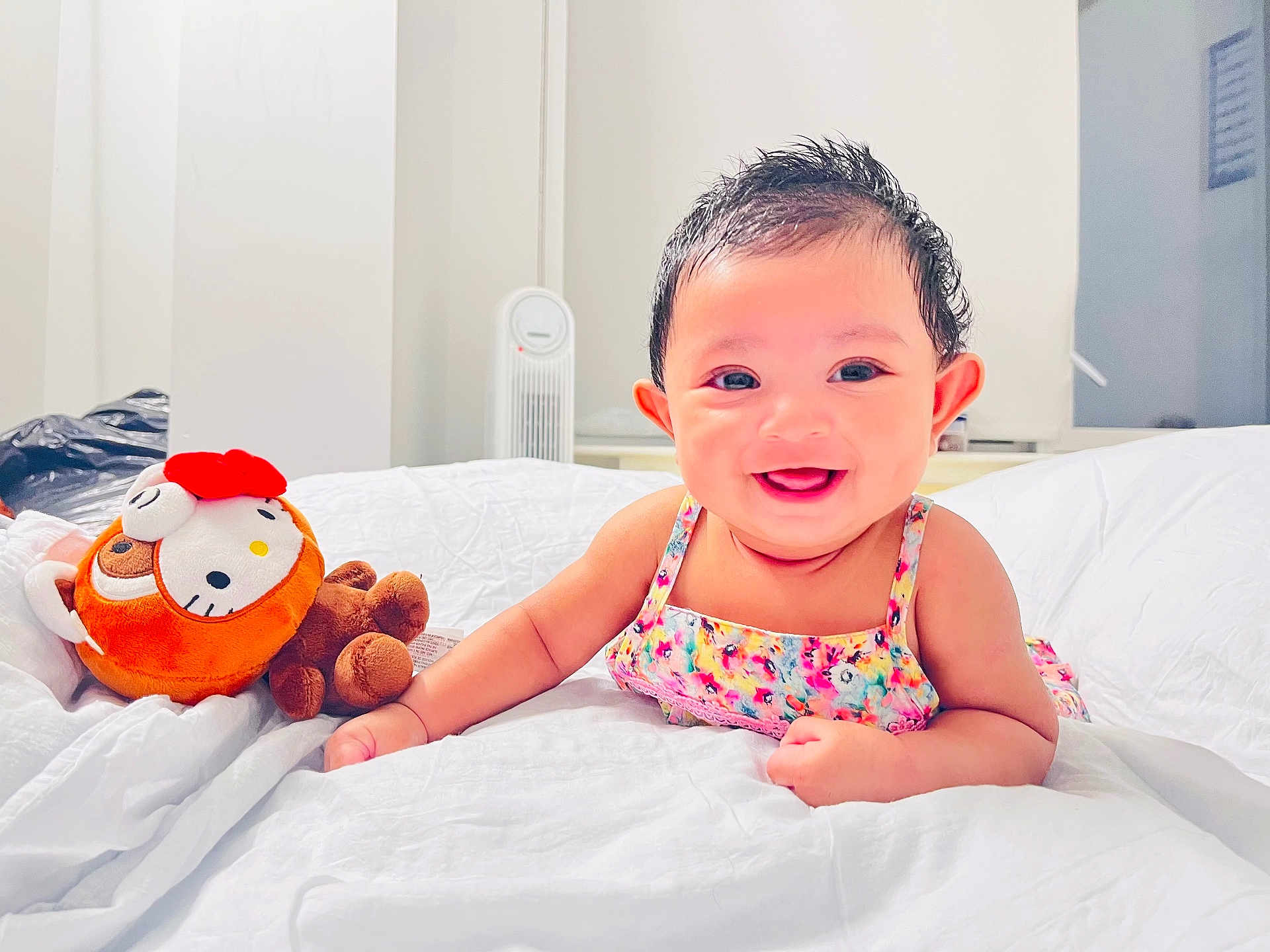 Jannatul joined the competition — help win amazing prizes! baby, smiling, child, plush_toy, bed, white_bedspread, colorful_dress, indoors, face, cute, happy, infant, portrait, toy, furniture, room, person, head, skin, young_child