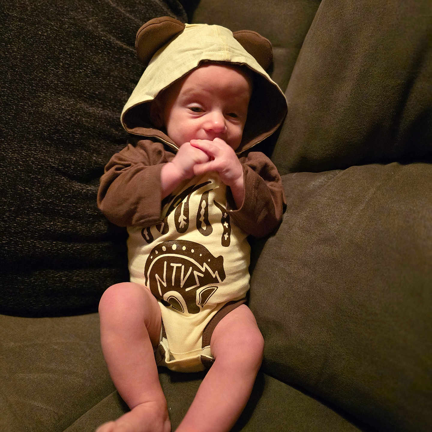 Desmond is registered to the contest to win money with this photo: baby, bear_ears, child, clothing, comfort, couch, cozy, cushion, cute, face, furniture, hands, hoodie, indoors, infant, legs, person, sitting, skin, soft