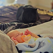 Desmond is registered to the contest to win money with this photo: baby, sleeping, pacifier, blanket, bed, cat, indoor, cozy, soft, infant, cute, rest, comfort, animal, pet, fur, peaceful, child, napping, warm