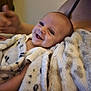 baby, smile, blanket, infant, person, happy, indoor, cozy, child, wrapped, soft_texture, human, portrait, cute, young, warmth, skin, face, expression, holding