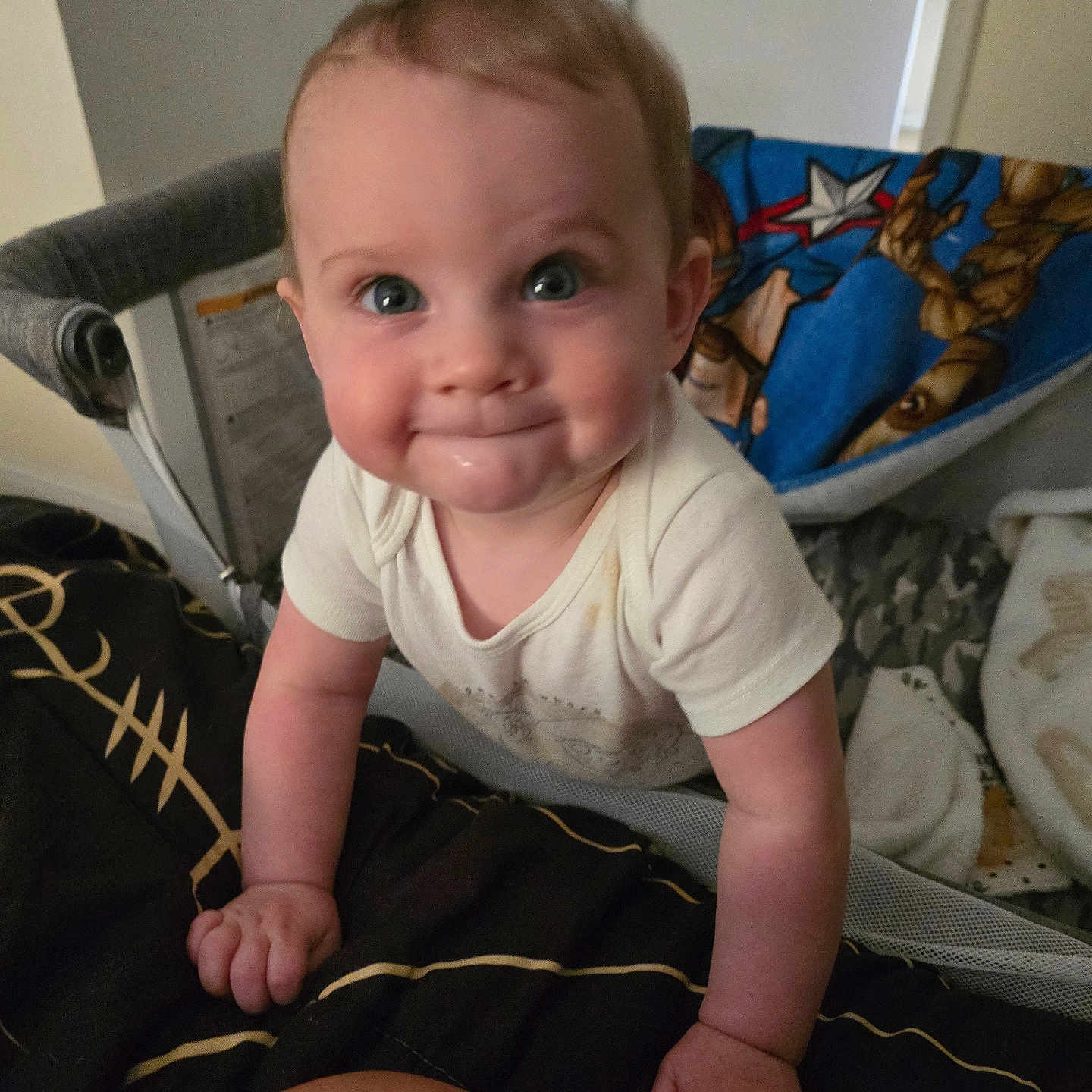 Desmond is registered to the contest to win money with this photo: baby, child, infant, smile, hands, blanket, bed, crib, person, cute, indoors, blue_blanket, white_shirt, face, eyes, skin, hair, expression, candid, closeup