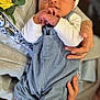 Hudson is registered to the contest to win money with this photo: baby, newborn, infant, sleeping, hands, hat, overalls, socks, person, holding, flower, yellow_flower, closeup, indoor, soft_light, warm_tone, portrait, caring, tenderness, cozy