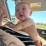 baby, child, infant, person, tattoo, striped_clothing, car_interior, window, sunlight, diaper, arm, face, holding, adult, skin, expression, seat, daylight, portrait, human