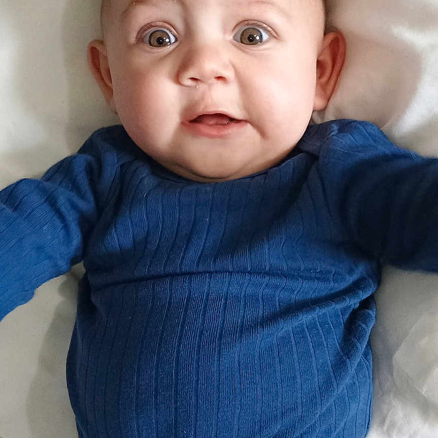 Jiraiya is registered to the contest to win money with this photo: baby, bear_pattern, blue_clothing, child, cozy, cute, face, head, indoors, infant, lying_down, pajamas, person, portrait, sleepwear, snowflake_pattern, surprised_expression, white_pillow, wide_eyes, young_child