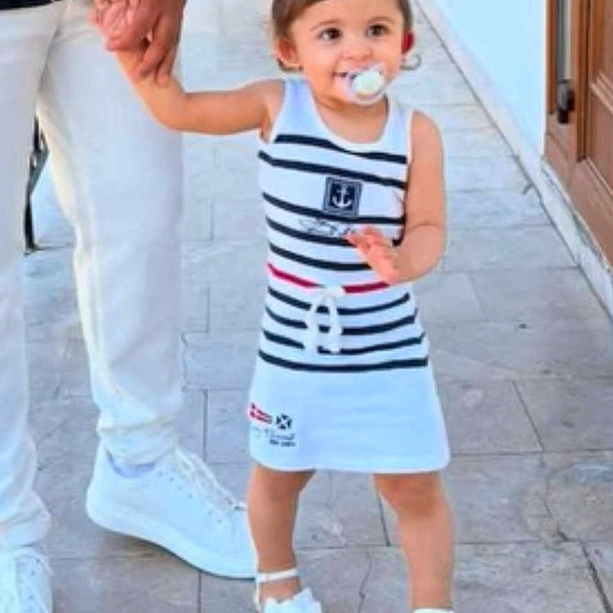 Tenessy a rejoint le concours — aidez-le/la à gagner de superbes lots ! adult, chair, child, door, dress, floor_tiles, footwear, hair_bows, happy, holding_hand, outdoor, pacifier, person, sidewalk, smiling, stripes, toddler, walking, white_shoes, young_child