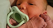 Elizabeth is registered to the contest to win money with this photo: newborn, baby, infant, child, face, pacifier, sleepy, eyes, hands, fingers, pink_clothing, onesie, cozy, portrait, close_up, indoors, blanket, adult_arm, cuddling, soft_lighting