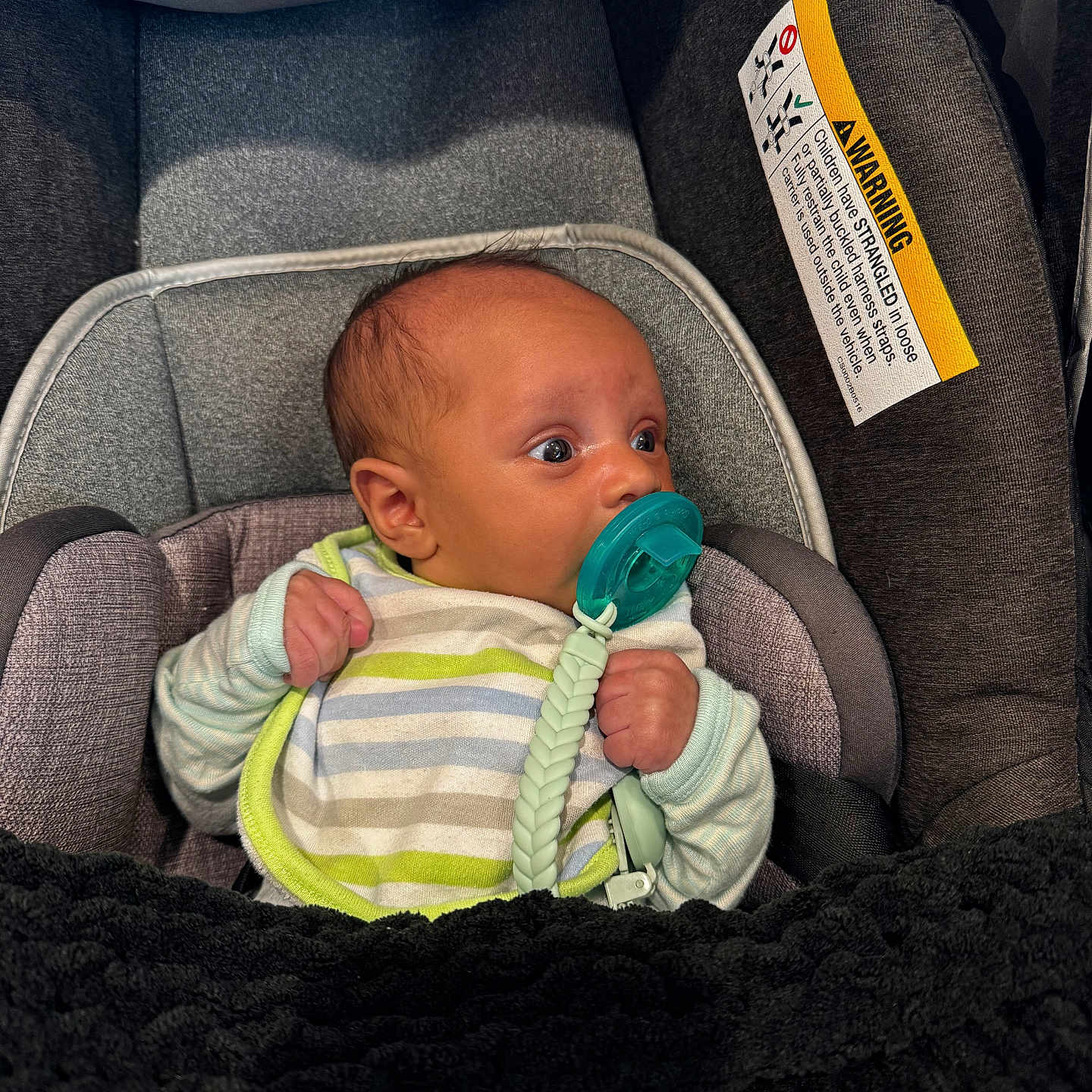 Carson is registered to the contest to win money with this photo: baby, infant, car_seat, pacifier, striped_clothing, blanket, cushion, child, cute, wide_eyes, cozy, indoor, soft, newborn, clothing, person, portrait, comfort, seat, wrapped