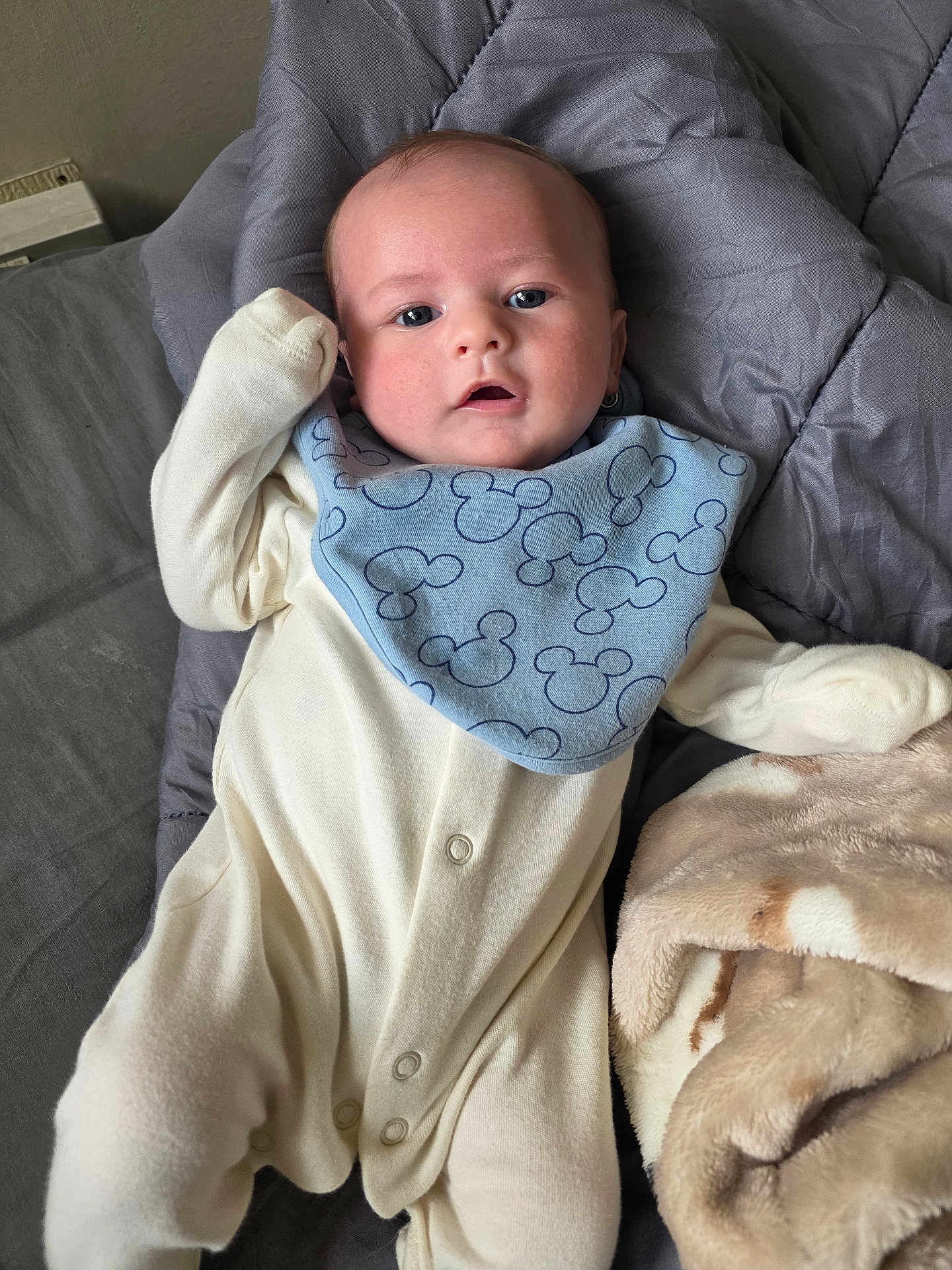 Oliver joined the competition — help win amazing prizes! baby, infant, onesie, bib, blue_bib, blanket, soft_texture, gray_quilt, beige_blanket, lying_down, face, eyes, hand, cute, child, indoors, portrait, clothing, person, comfort