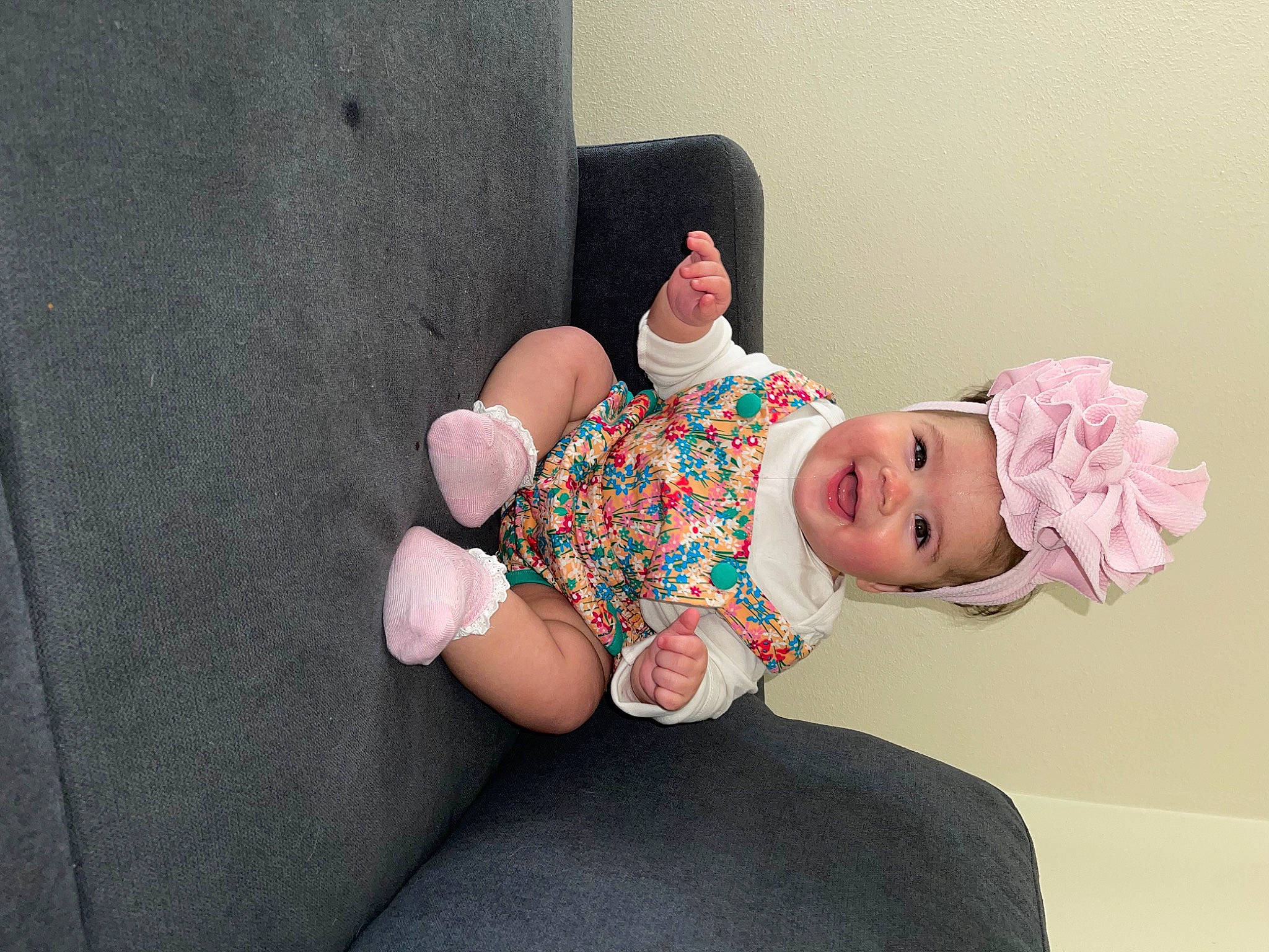 Evelyn is registered to the contest to win money with this photo: baby, baby_toddler_clothing, child, comfort, foot, fun, gesture, happy, headwear, human_leg, linens, person, pink, room, sitting, skin, sleeve, sock, thigh, thumb