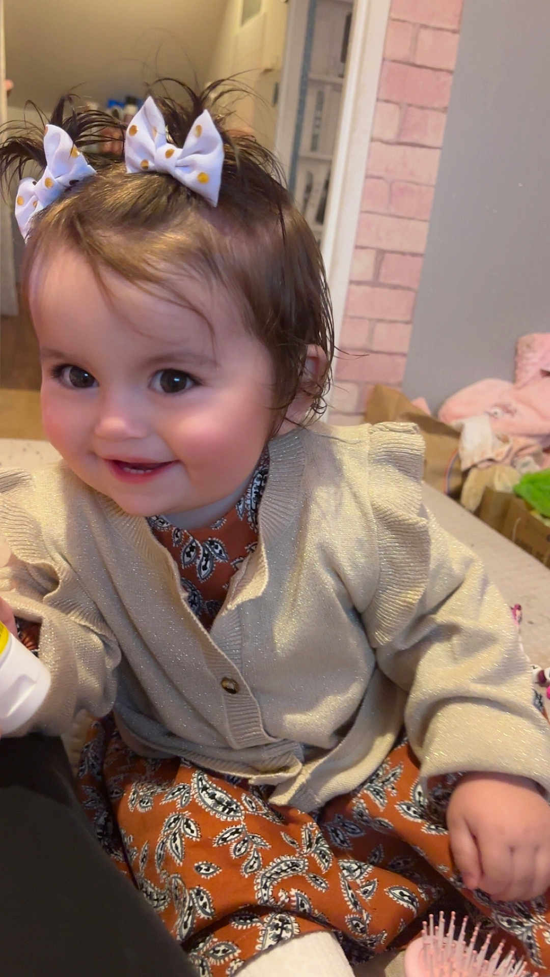 Syanna a rejoint le concours — aidez-le/la à gagner de superbes lots ! toddler, child, smile, indoor, hair_bows, pigtails, cardigan, patterned_clothing, face, hand, hairbrush, furniture, cozy, happy, cute, person, baby, home, sitting, playful