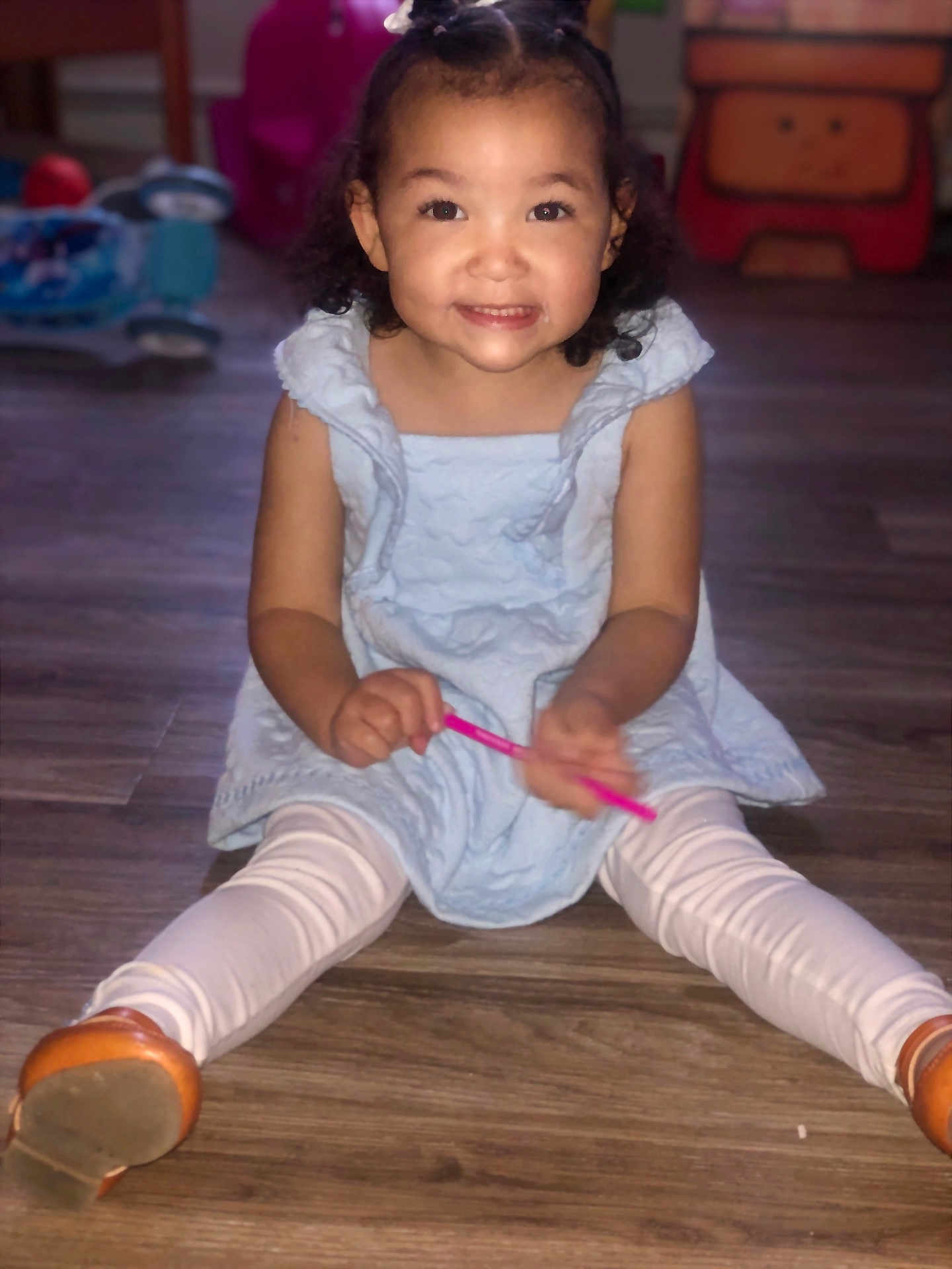 Kamara joined the competition — help win amazing prizes! child, girl, smiling, sitting, blue_dress, white_leggings, brown_shoes, wooden_floor, indoor, toy, happy, face, person, curly_hair, holding, pink_object, playful, cute, young, portrait
