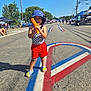 Kamara joined the competition — help win amazing prizes! child, toddler, water_gun, hat, shorts, crocs, street, road_painting, patriotic_colors, red, white, blue, sunny_day, outdoor, festival, people, trees, sidewalk, summer, fun