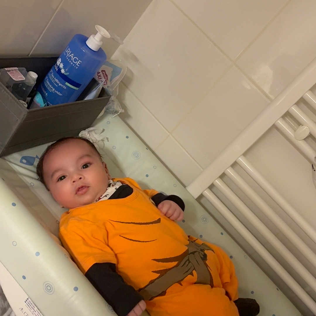 Ishaq participe au concours pour gagner de l'argent avec cette photo : baby, baby_bottle, baby_care, baby_products, baby_wipes, bathroom, black_socks, changing_pad, child, container, cute, diapers, indoor, infant, newborn, orange_clothing, person, resting, soft_lighting, tiled_wall