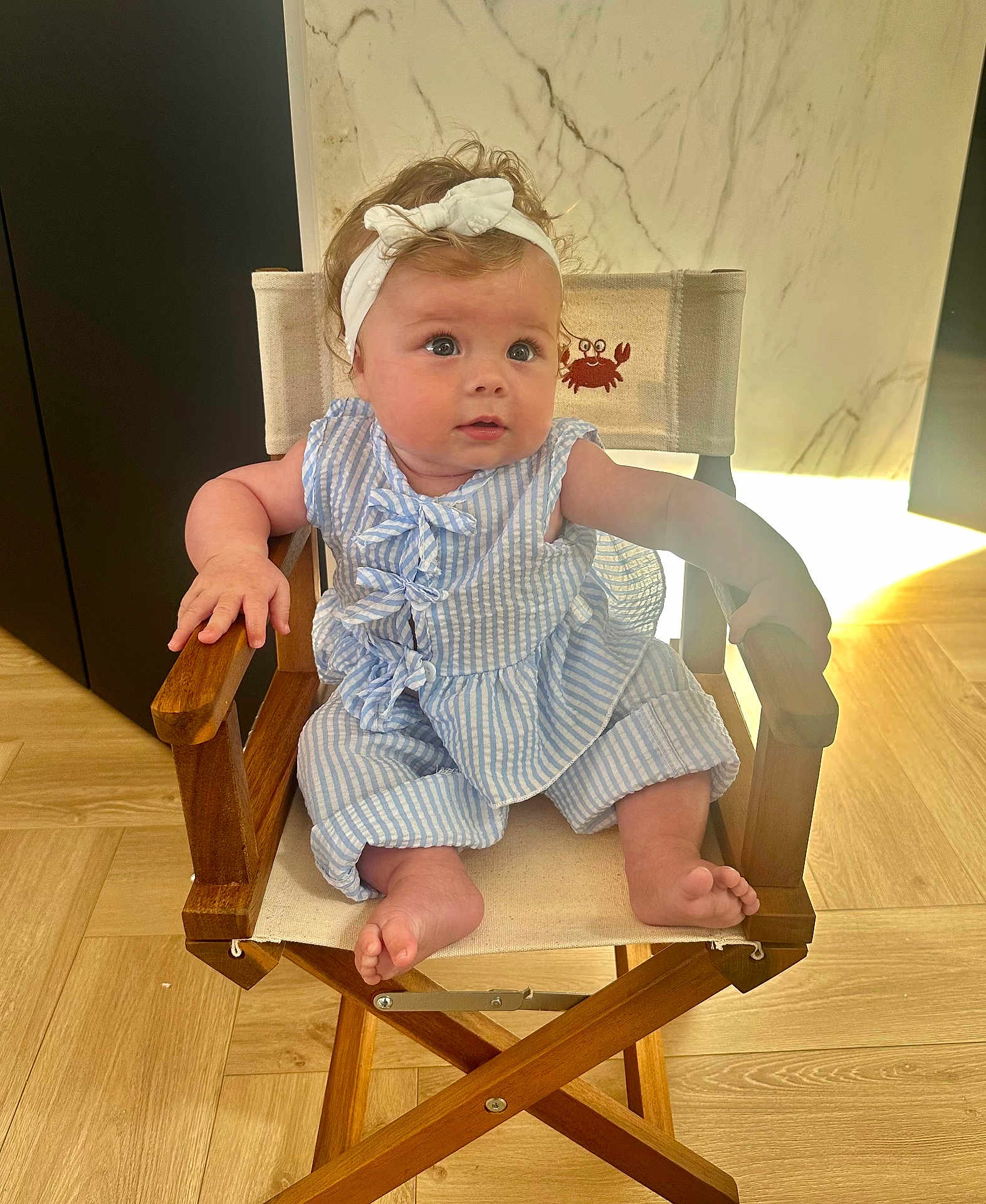 Agathe participe au concours pour gagner de l'argent avec cette photo : baby, child, infant, sitting, wooden_chair, headband, bow, blue_outfit, striped_clothing, curious_expression, indoor, marble_wall, wooden_floor, cute, small_feet, hand_on_armrest, comfortable, portrait, young_child, adorable